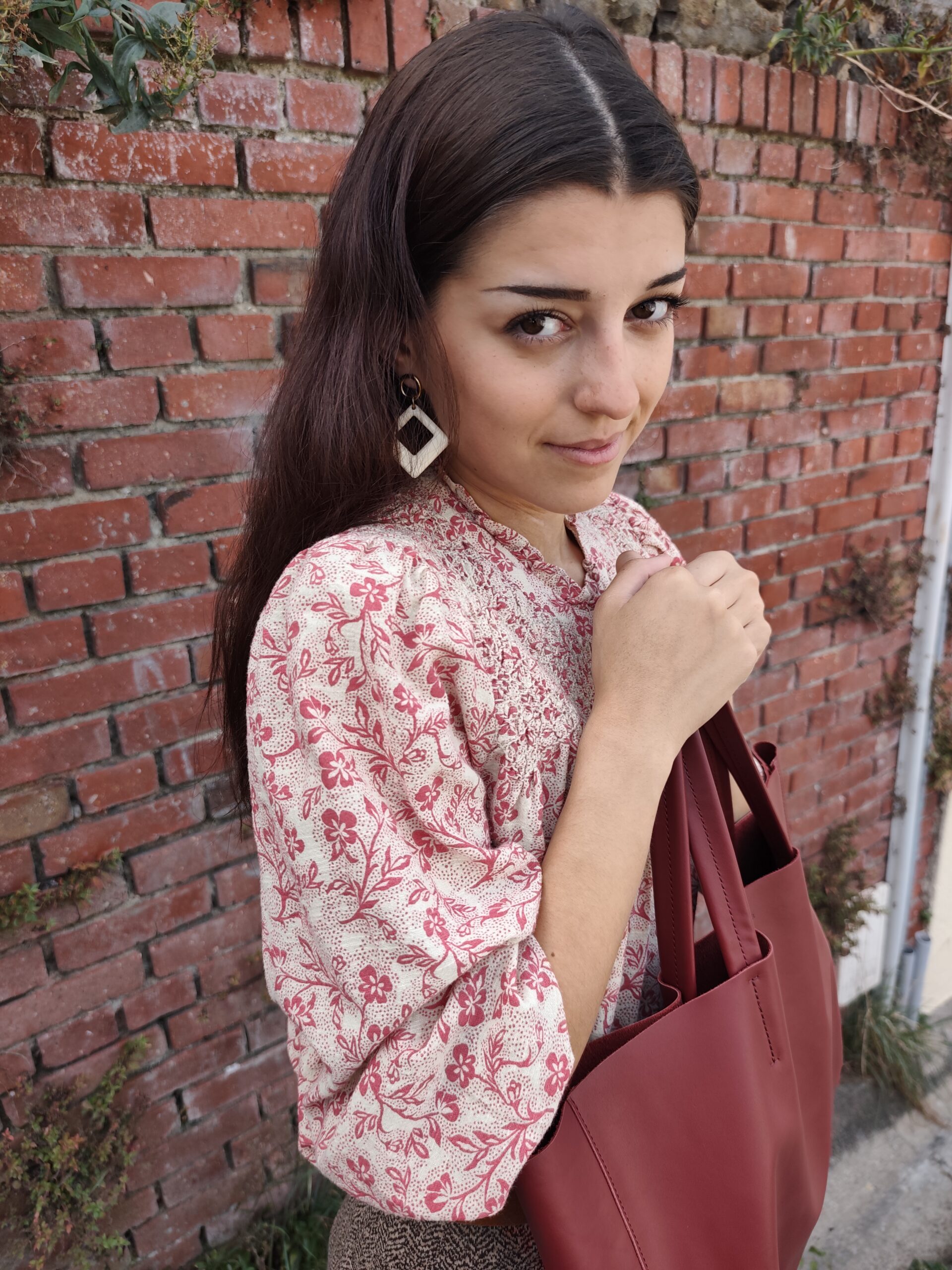Blouse à motifs floraux et cabas en cuir grenade, devant un mur de briques