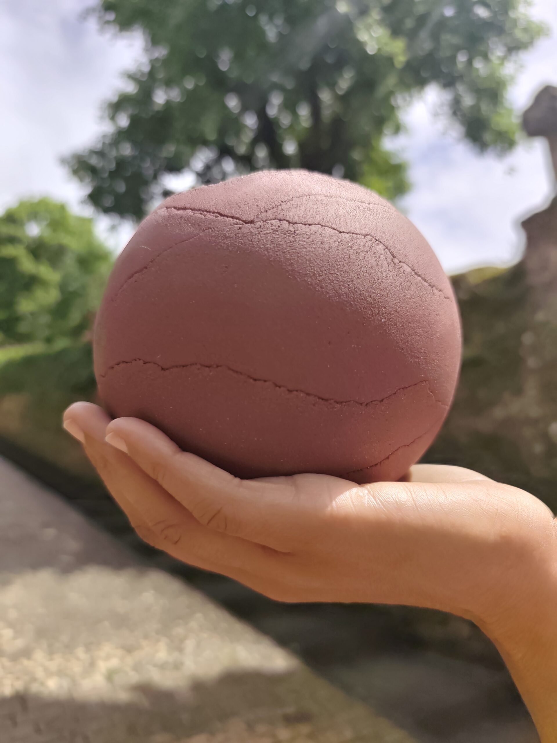 Sphère en céramique rose craquelée posée dans une main, en extérieur
