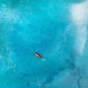 Sieste océane, tableau de Nathalie Bonetti : une surfeuse allongée sur sa planche dérive sur une eau turquoise